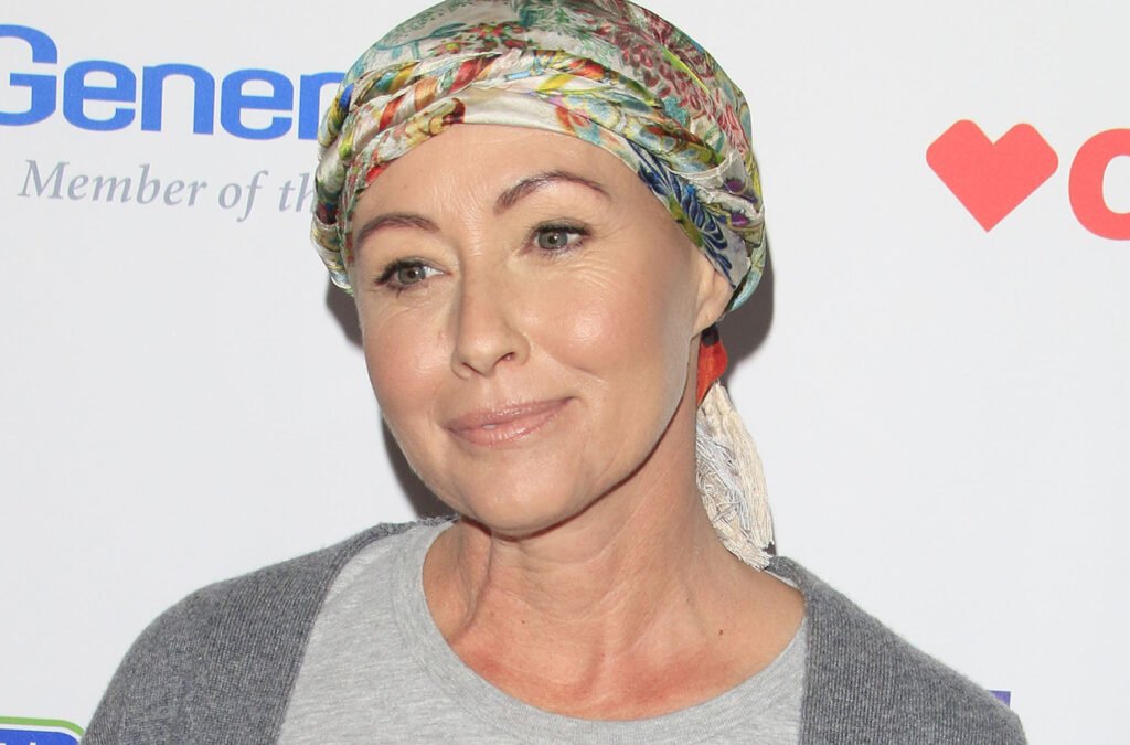 Shannen Doherty smiling at a stand up for cancer event wearing a colorful scarf on her head.