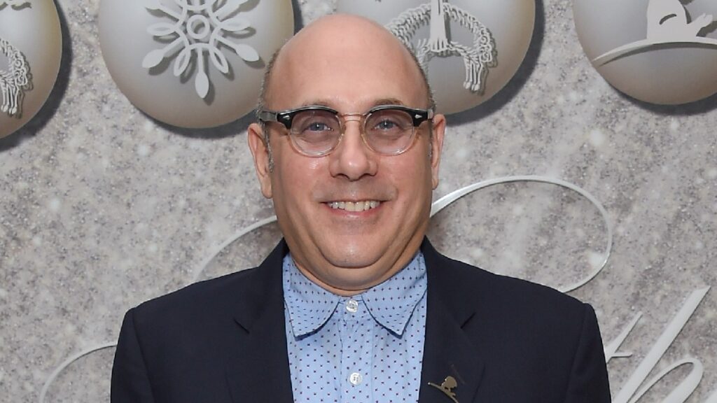 Willie Garson wears a blue shirt and dark suit jacket against a gray background