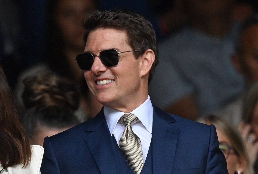 Tom Cruise smiling in a blue suit and black sunglasses