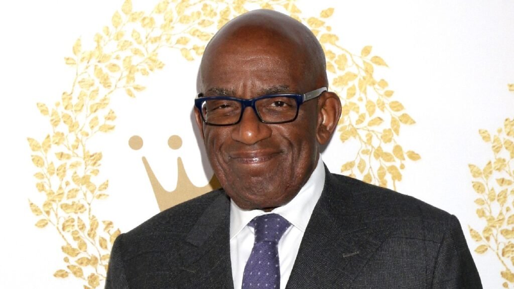 Al Roker wears a dark suit against a white and gold background on the red carpet