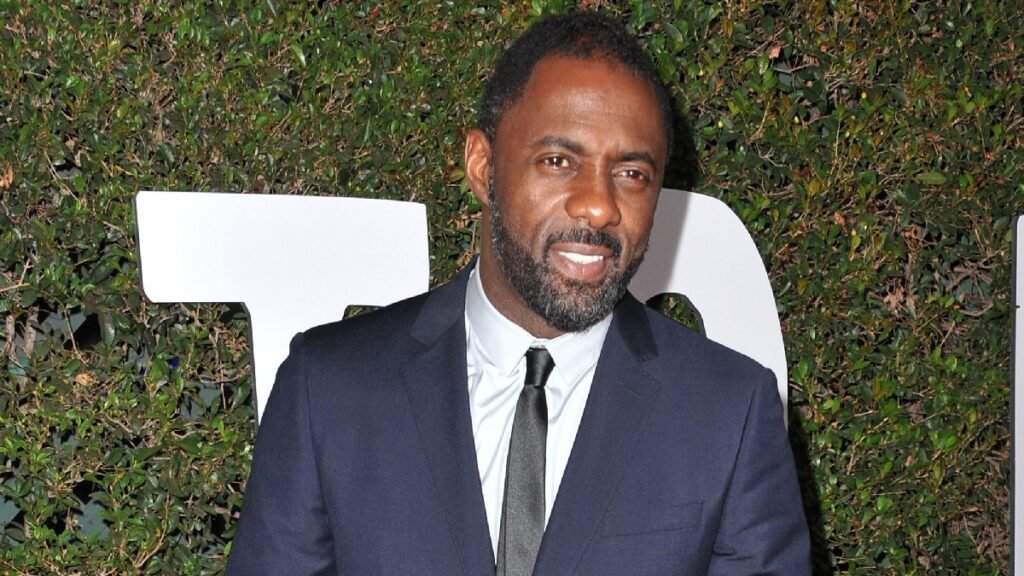 Idris Elba wears a dark suit in front of a leafy green background