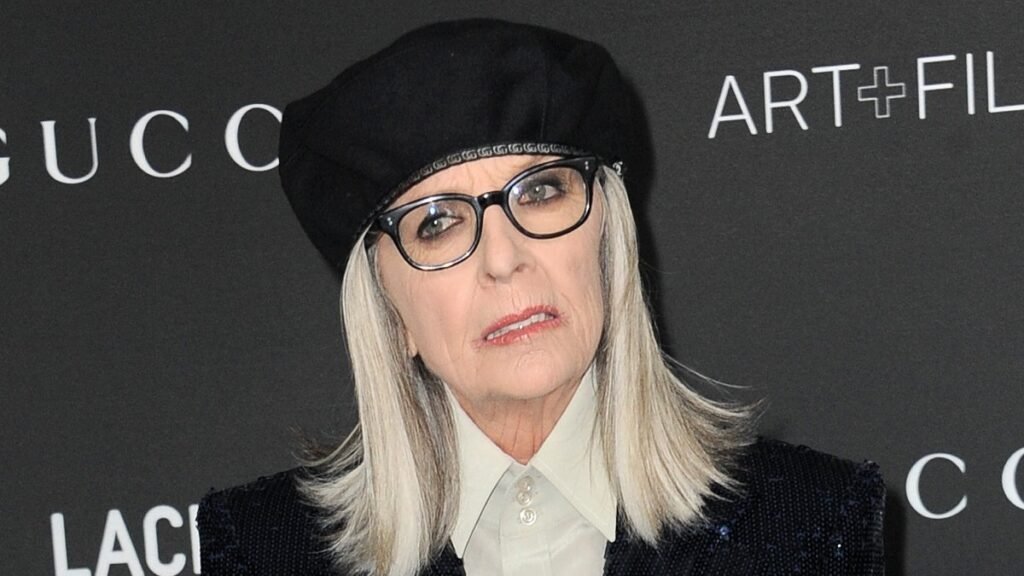 Diane Keaton wears a sparkly blue pantsuit over a white top with a black hat on the red carpet