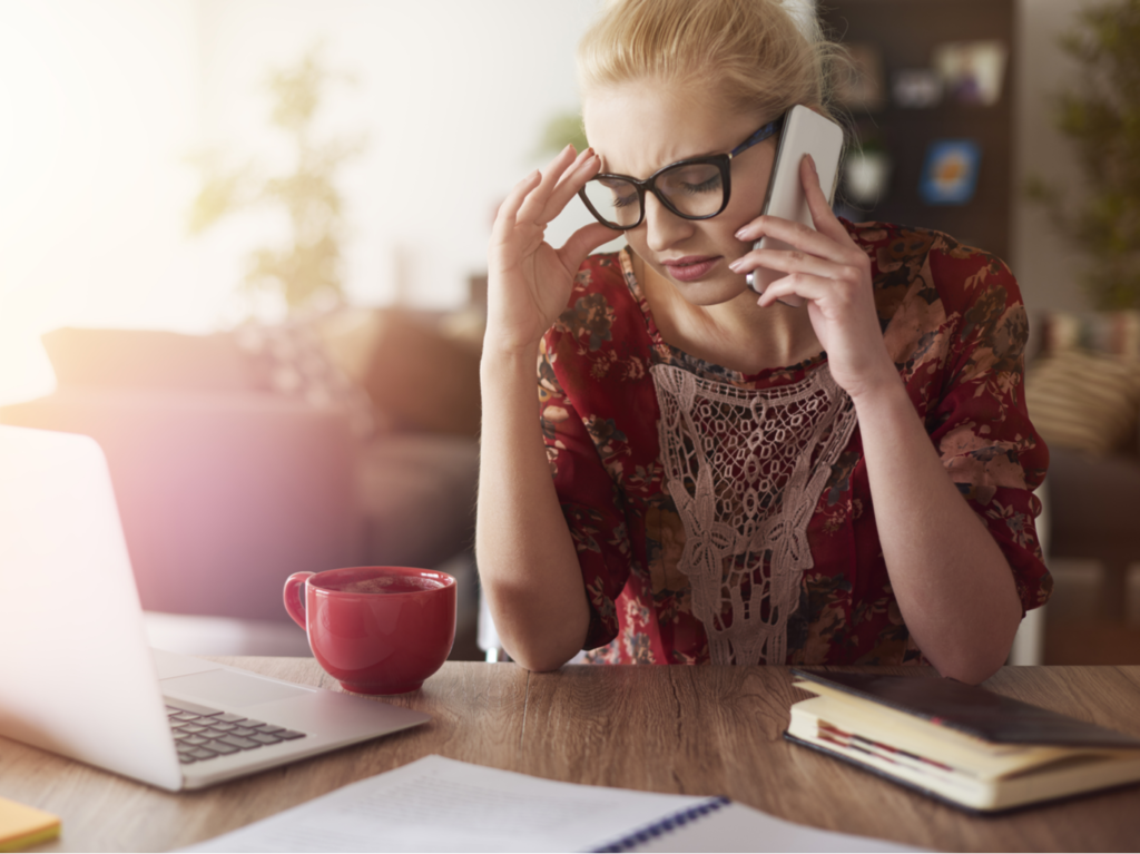 A frustrated woman is holding a cellphone to her ear and waiting on hold