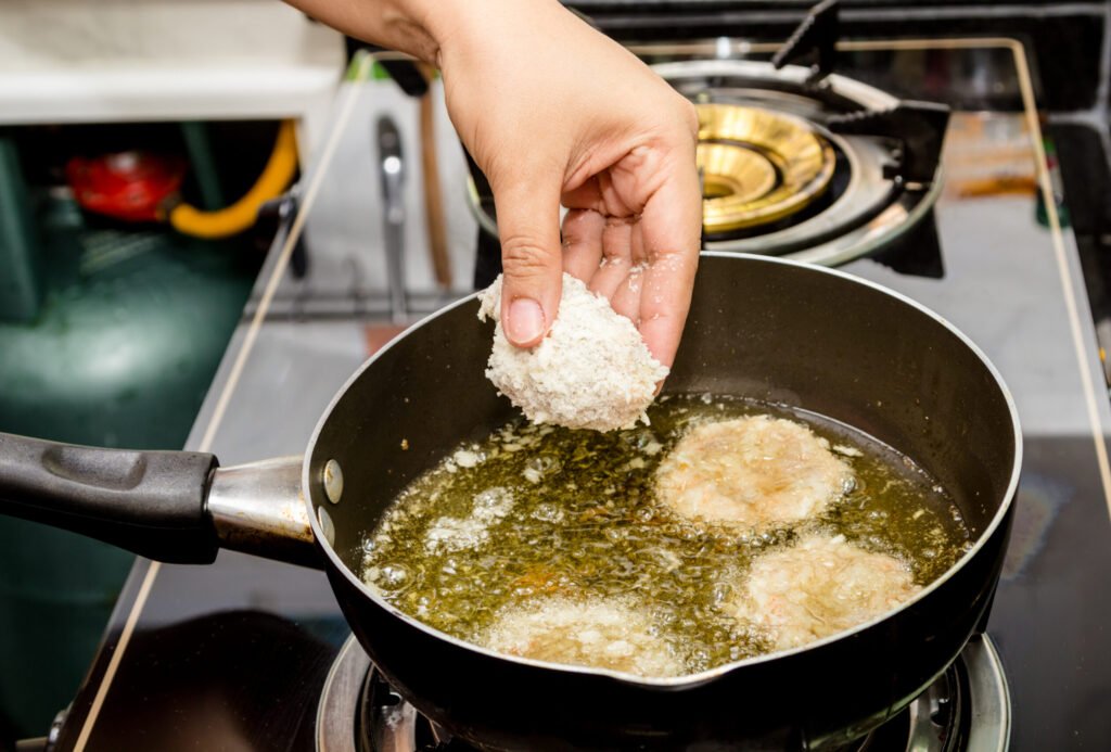 Close up of a home cook deep drying food in a pan of hot oil.