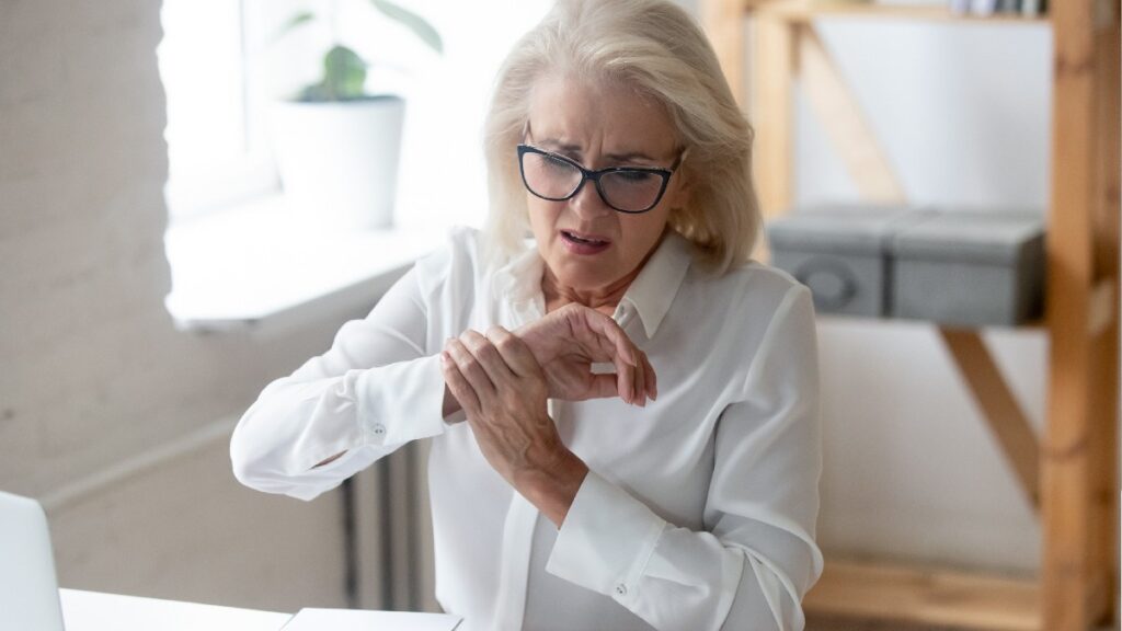 A woman wearing a white shirt and glasses holds up an injured wrist indoors