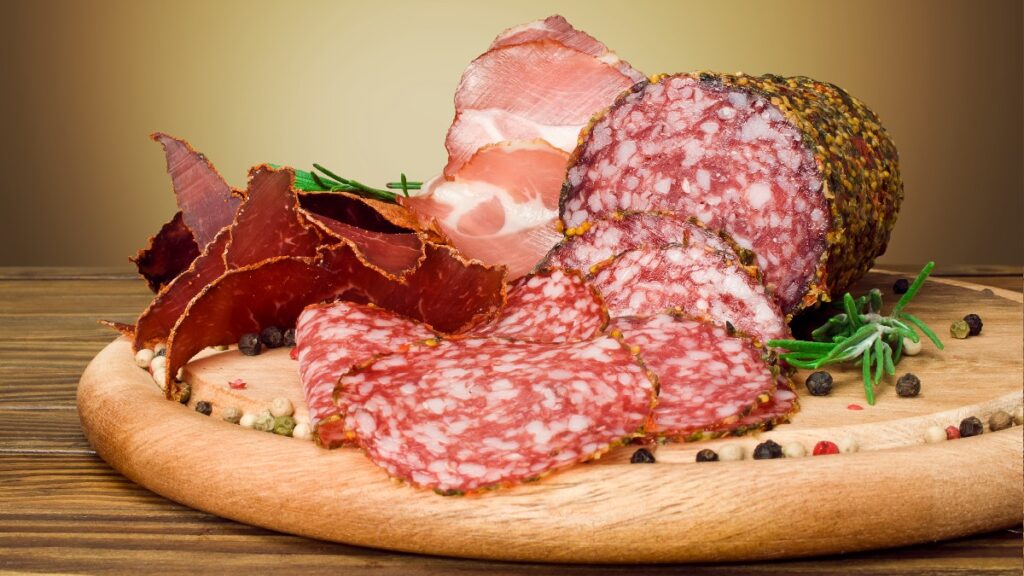 A charcuterie board filled with varied meets sits on a wooden table in front of a gold background