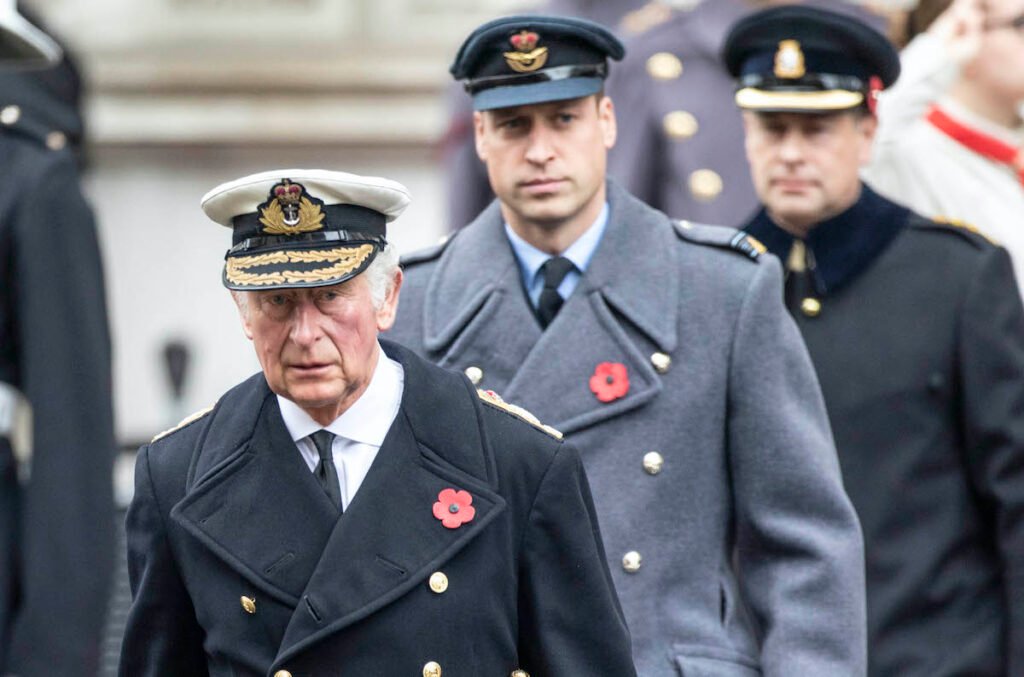 Prince William in a grey suit behind Prince Charles in a grey suit