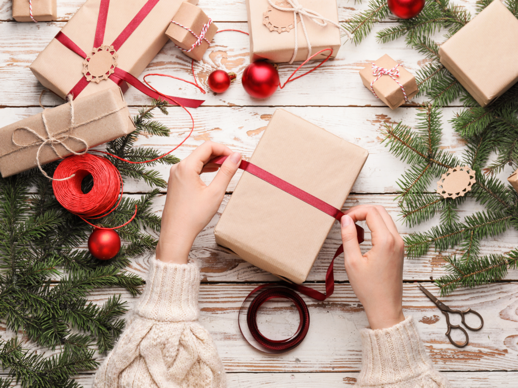 Two hands wrapping a ribbon around a gift, with more presents in the background