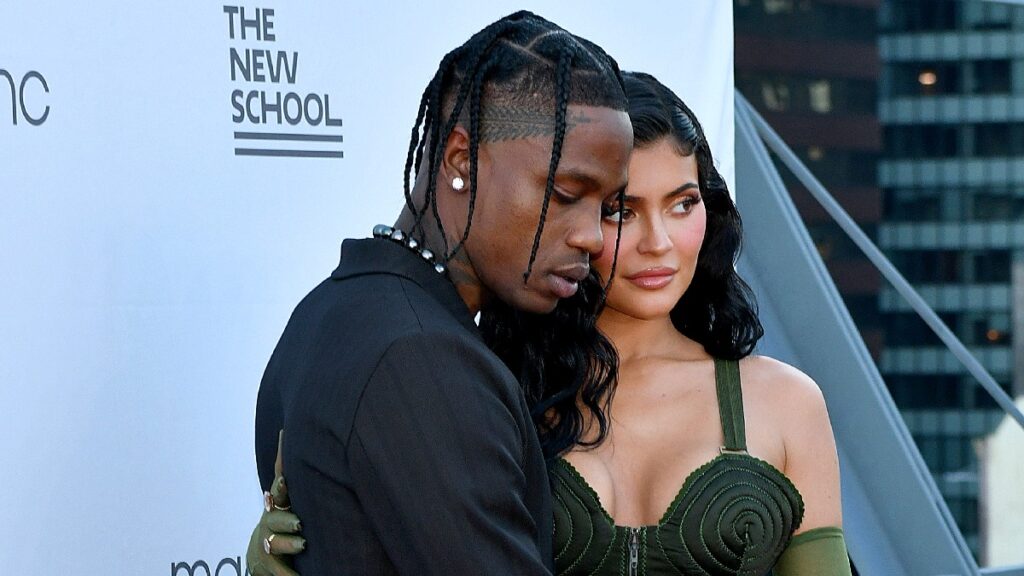 Travis Scott wears a black outfit and poses with Kylie Jenner, in a green dress, on the red carpet