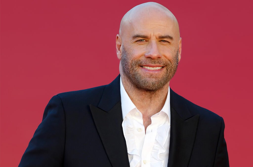 John Travolta smiling in front of a red background