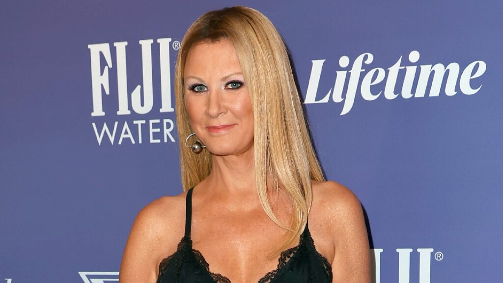 Sandra Lee wears a dark dress on the red carpet in front of a blue background