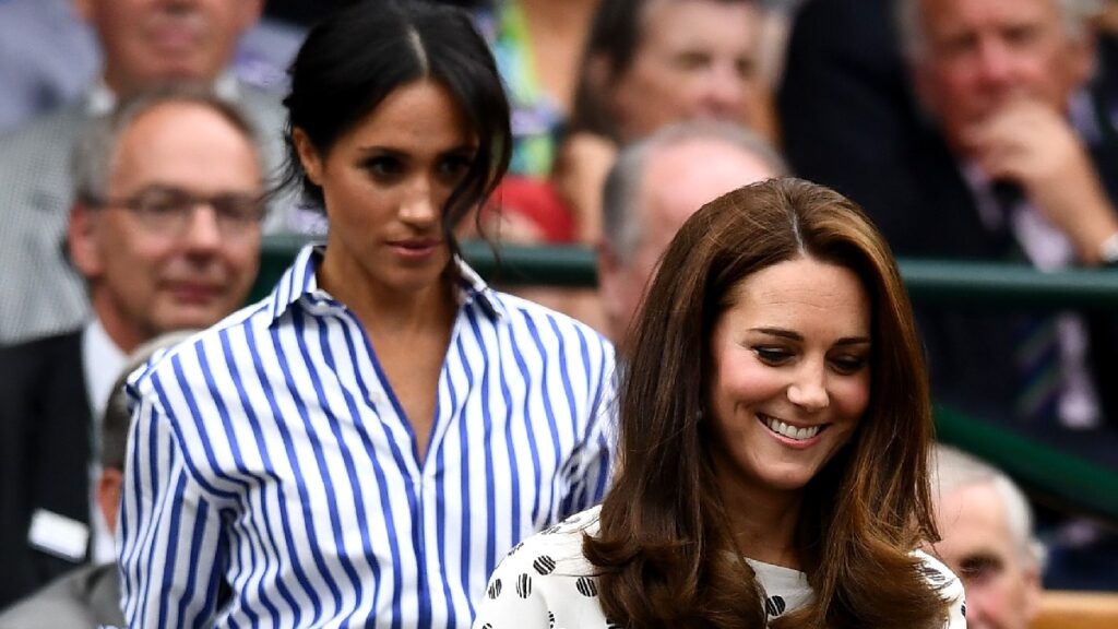 Meghan Markle, wearing a blue stripped top, follows Kate Middleton, in a cream colored dress, down the stairs of Wimbledon