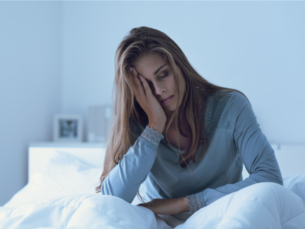 A woman sits up in bed and rubs her face after a night of poor sleep