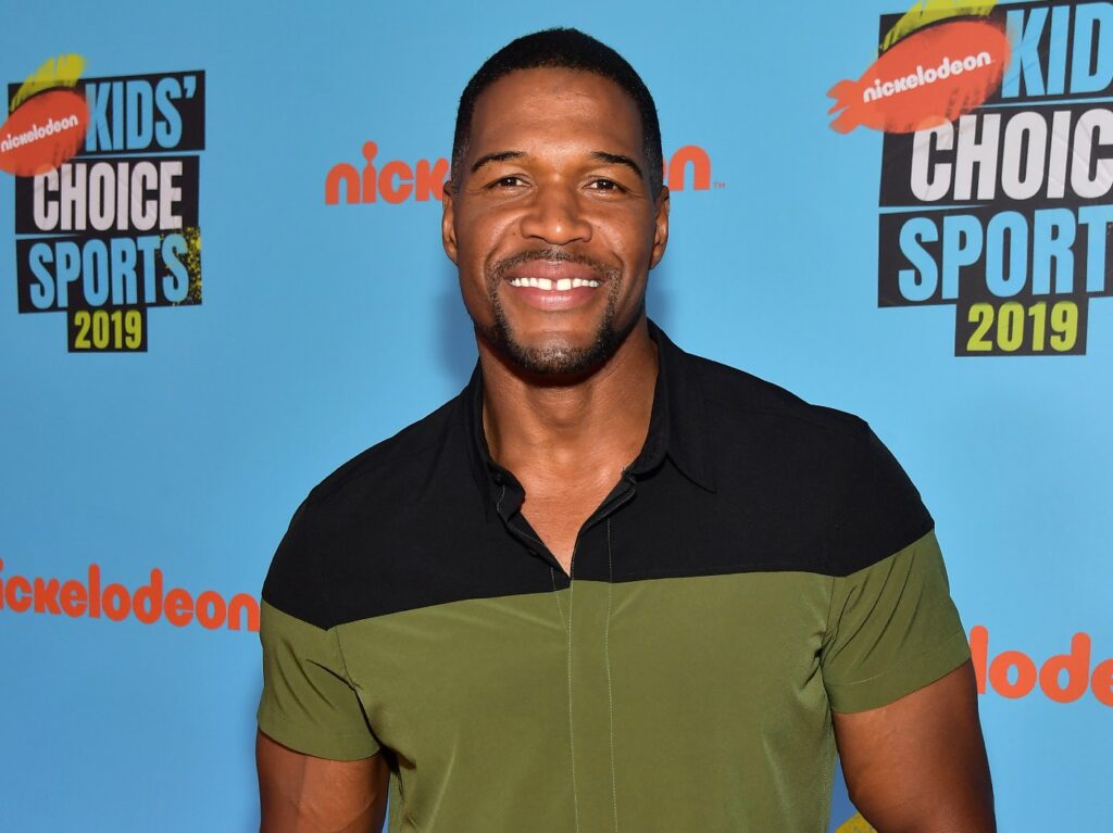 Michael Strahan smiles wearing green and black dress shirt