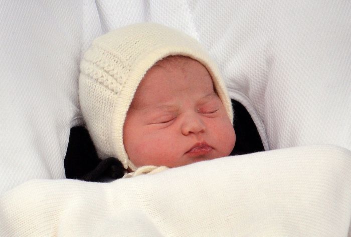 A young baby sleeps under blankets, wearing a cream colored hat