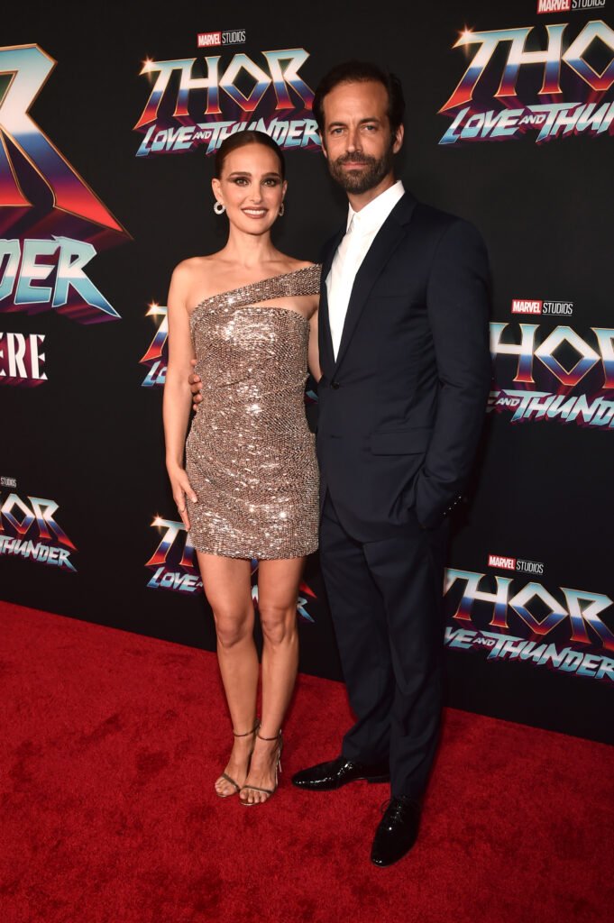 (L-R) Natalie Portman, wearing gold sparkle dress and Benjamin Millepied wearing classic black suit against black background