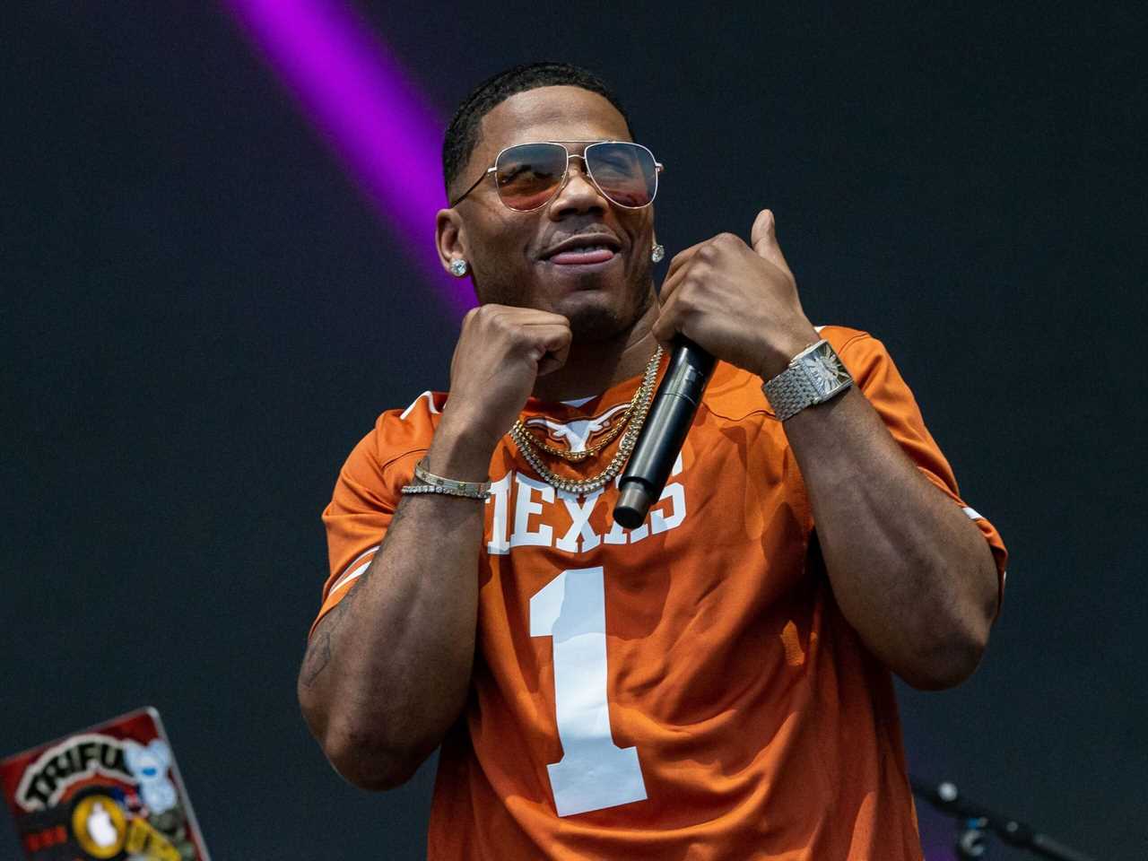 Nelly posing onstage with two fists up to his face. He is wearing an orange Broncos jersey