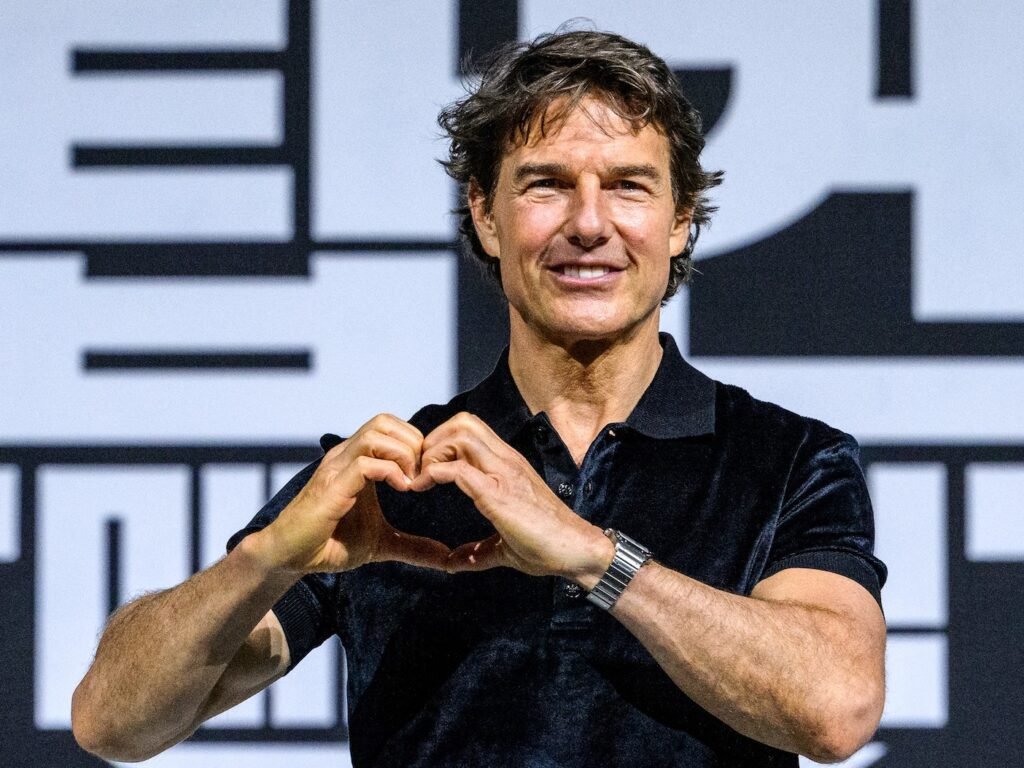 Tom Cruise in a black shirt making a heart with his hands