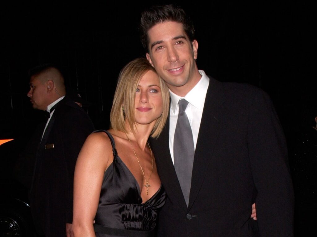 Jennifer Aniston, in a black dress, poses next to David Schwimmer, in a dark suit, on the red carpet