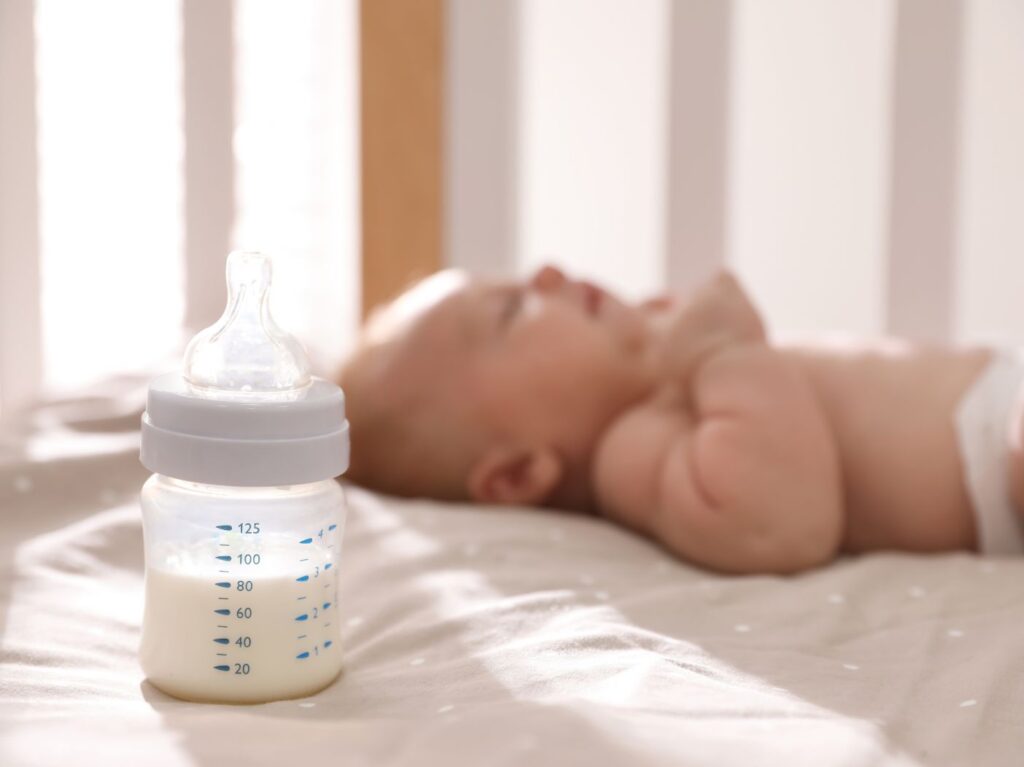 Newborn baby sleeping in background, focus on bottle of milk