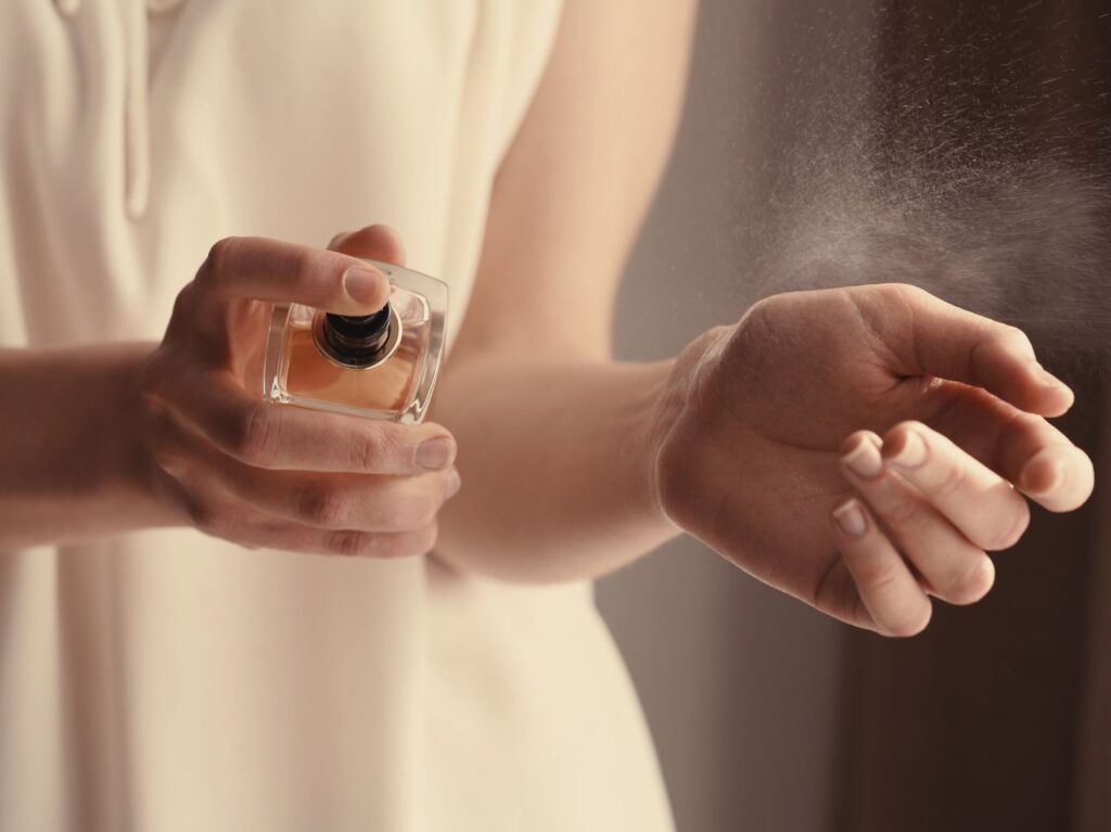 Closeup of woman's hands, one hand spraying perfume on her wrist