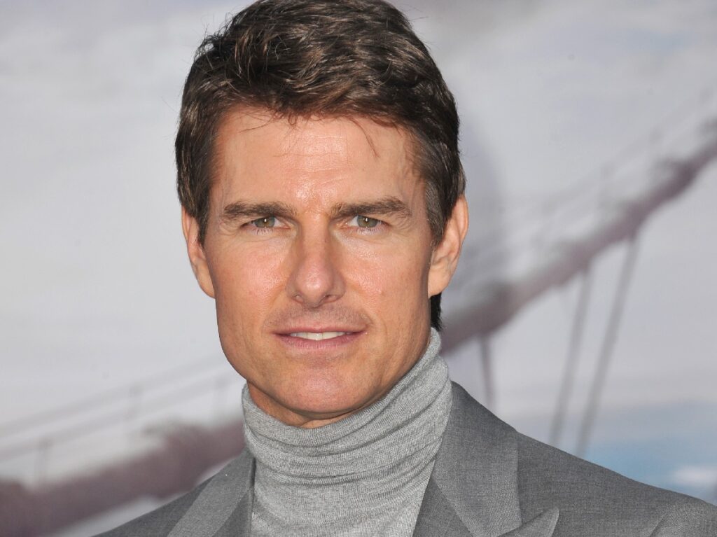 Tom Cruise wears a gray suit jacket over a gray turtleneck on the red carpet