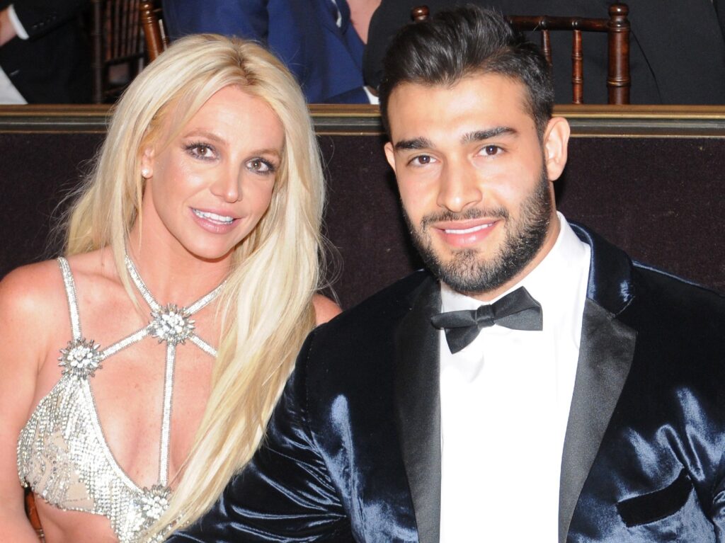 Britney Spears (L) in silver dress sitting next to Sam Asghari, who is wearing a dark blue suit jacket and bowtie