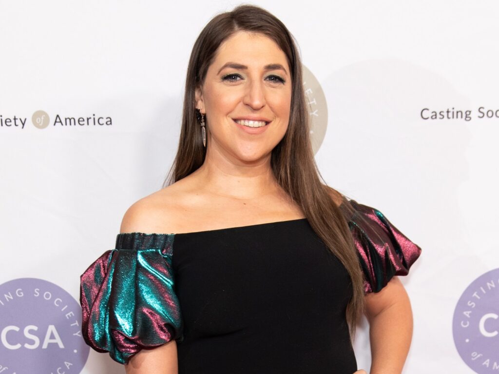 Mayim Bialik smiling in black dress with puffy sleeves