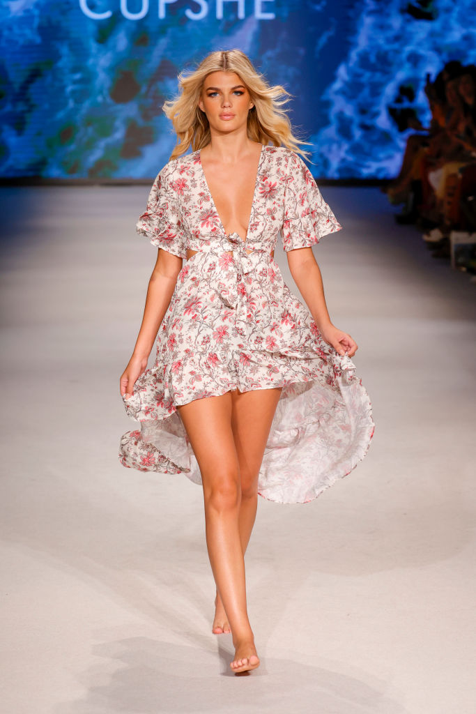 A model walks the runway in a floral, flowy high-low dress. 