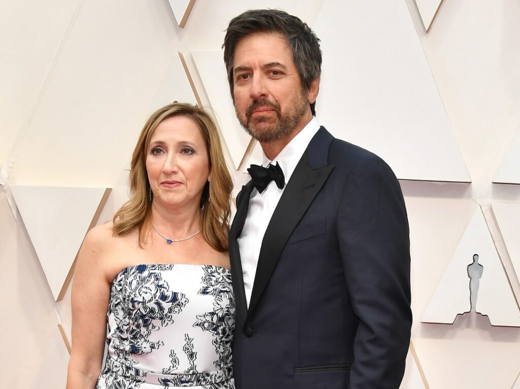 Ray Romano (R) in classic black suit and tie standing next to his wife Anna Romano, who is wearing a strapless white gown with black print