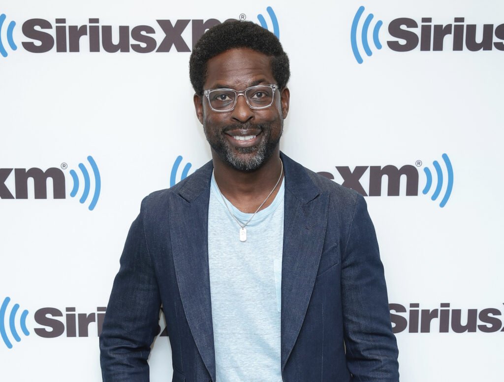 Sterling K Brown smiling in a navy jacket and light blue shirt