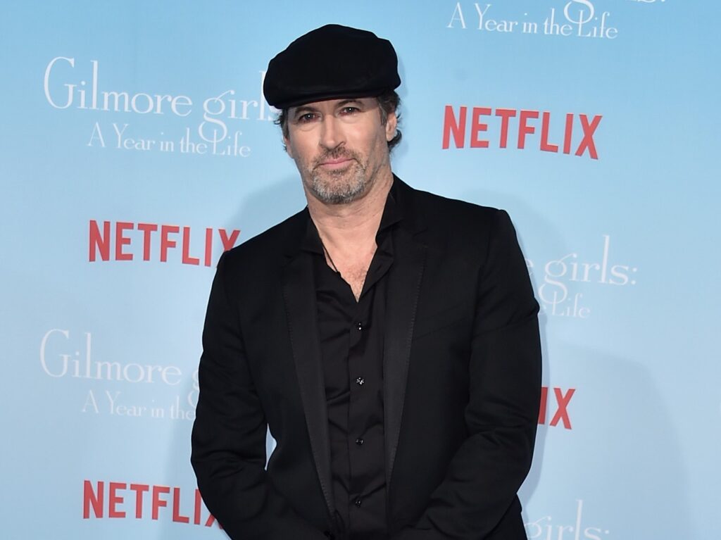 Scott Patterson in black suit with black hat against sky blue backdrop