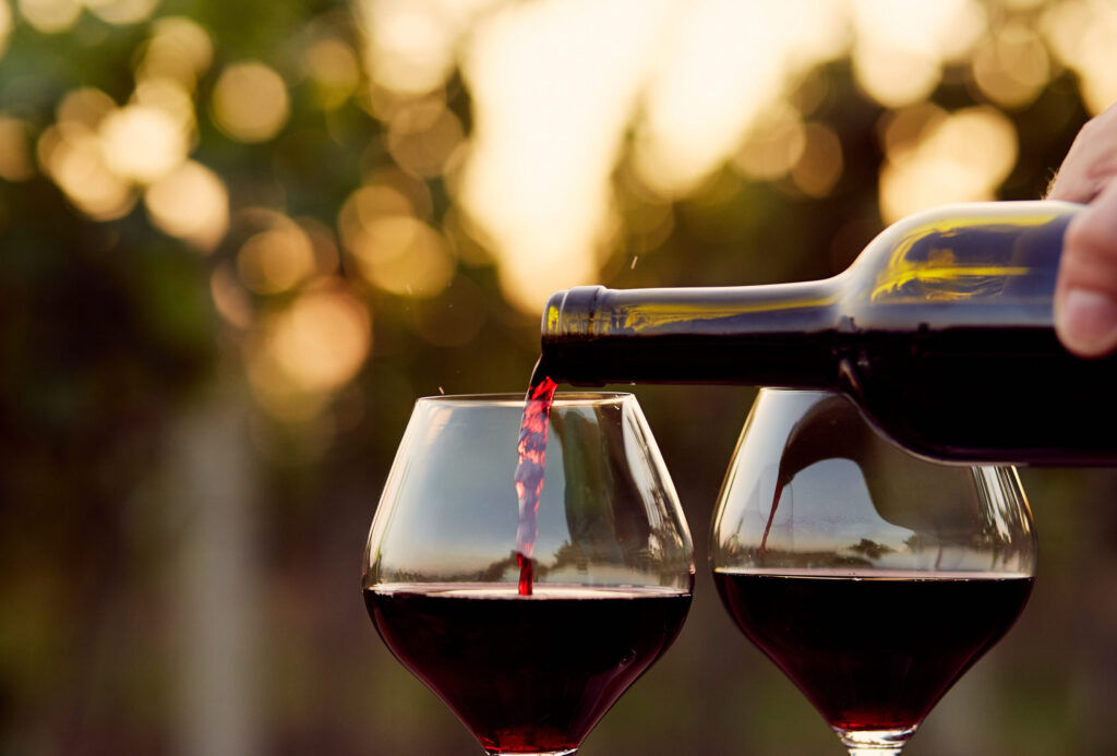 A bottle of red win being poured into two wine glasses