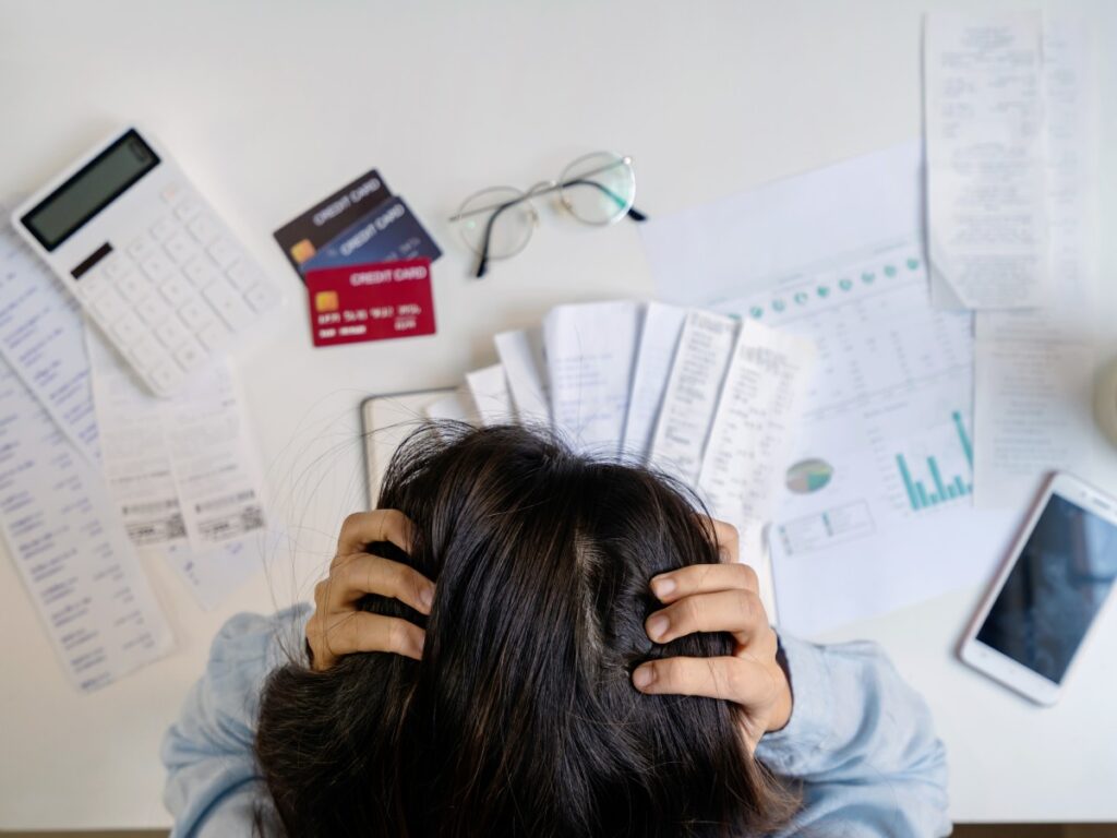 Aerial view of woman holding her head in her hands while looking at a table full of bills