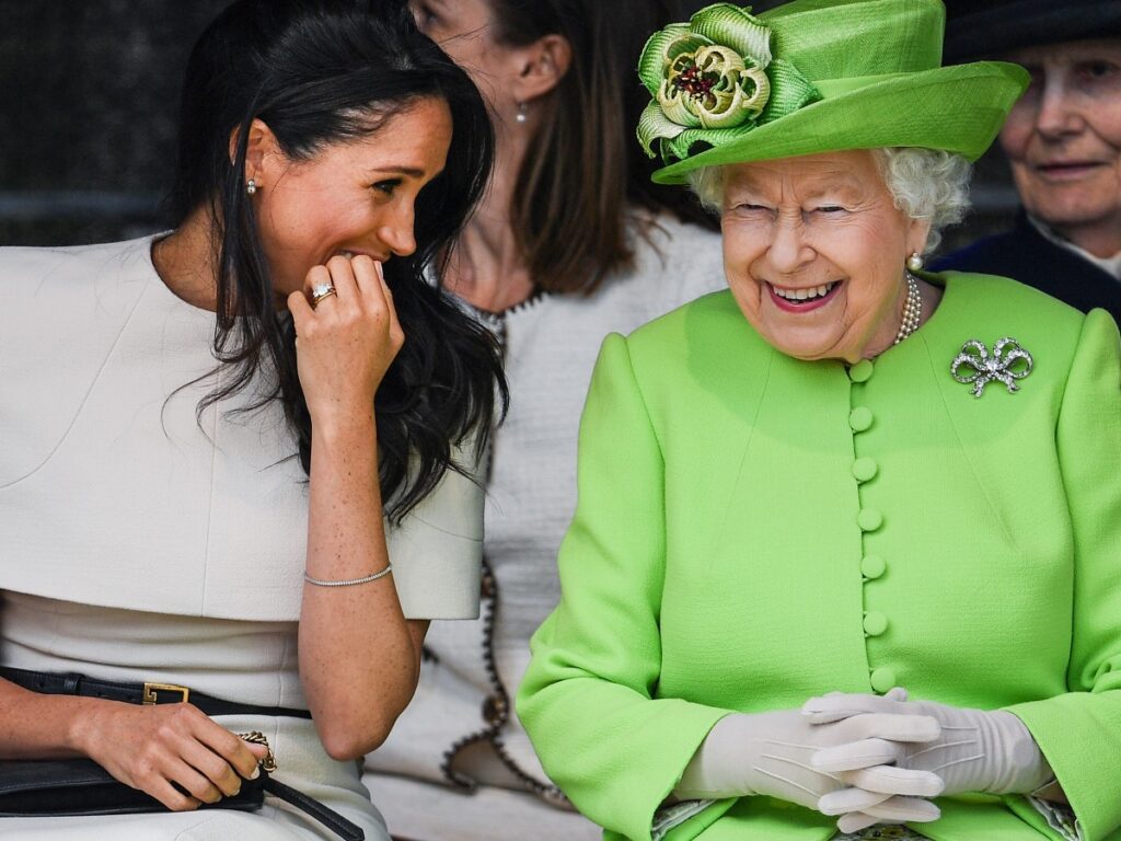 Meghan Markle (L)in white dress smiling next to Queen Elizabeth, who is wearing a neon green suit and hat