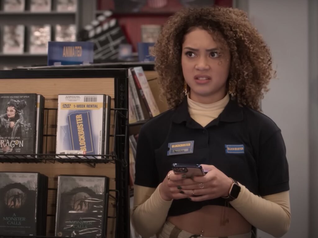 screenshot from Blockbuster showing DVDs on shelves and an employee in a uniform shirt