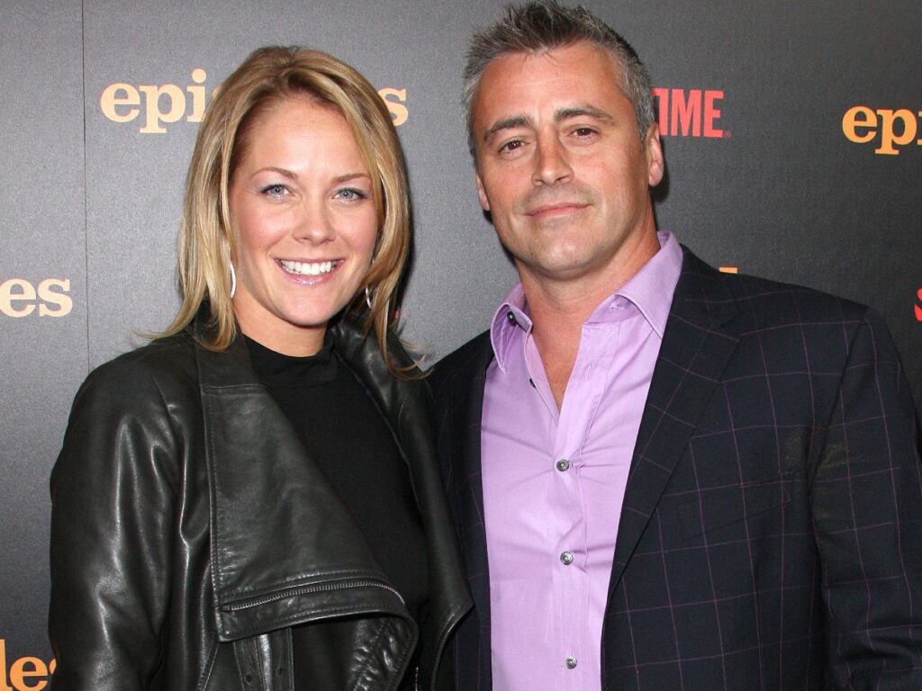 Melissa McKnight (L) in black leather jacket smiling next to Matt LeBlanc, who is wearing a purple dress shirt and black jacket