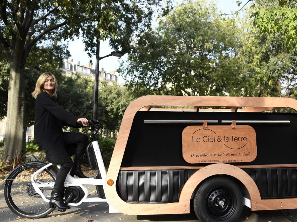 Blonde Woman on bike pushing hearse down the street